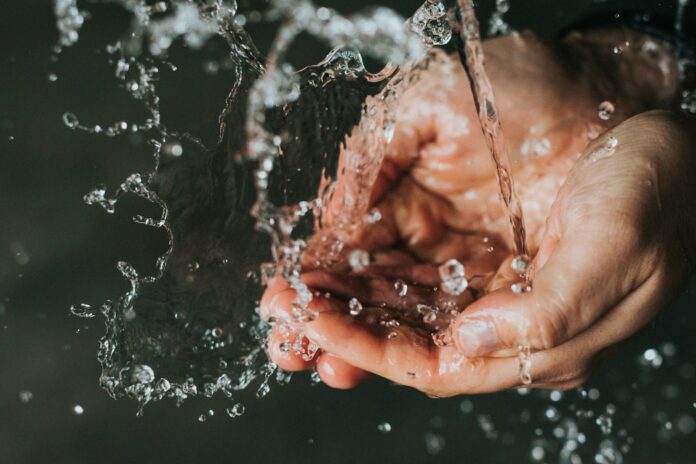 Photo by Nathan Dumlao a person holding their hands under a stream of water