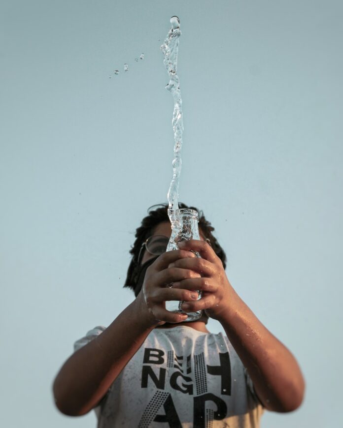 Photo by Amaan Ali man in black and white crew neck t-shirt holding water fountain