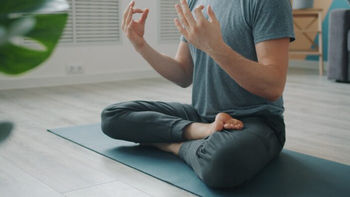 Man meditating in lotus pose on yoga mat.